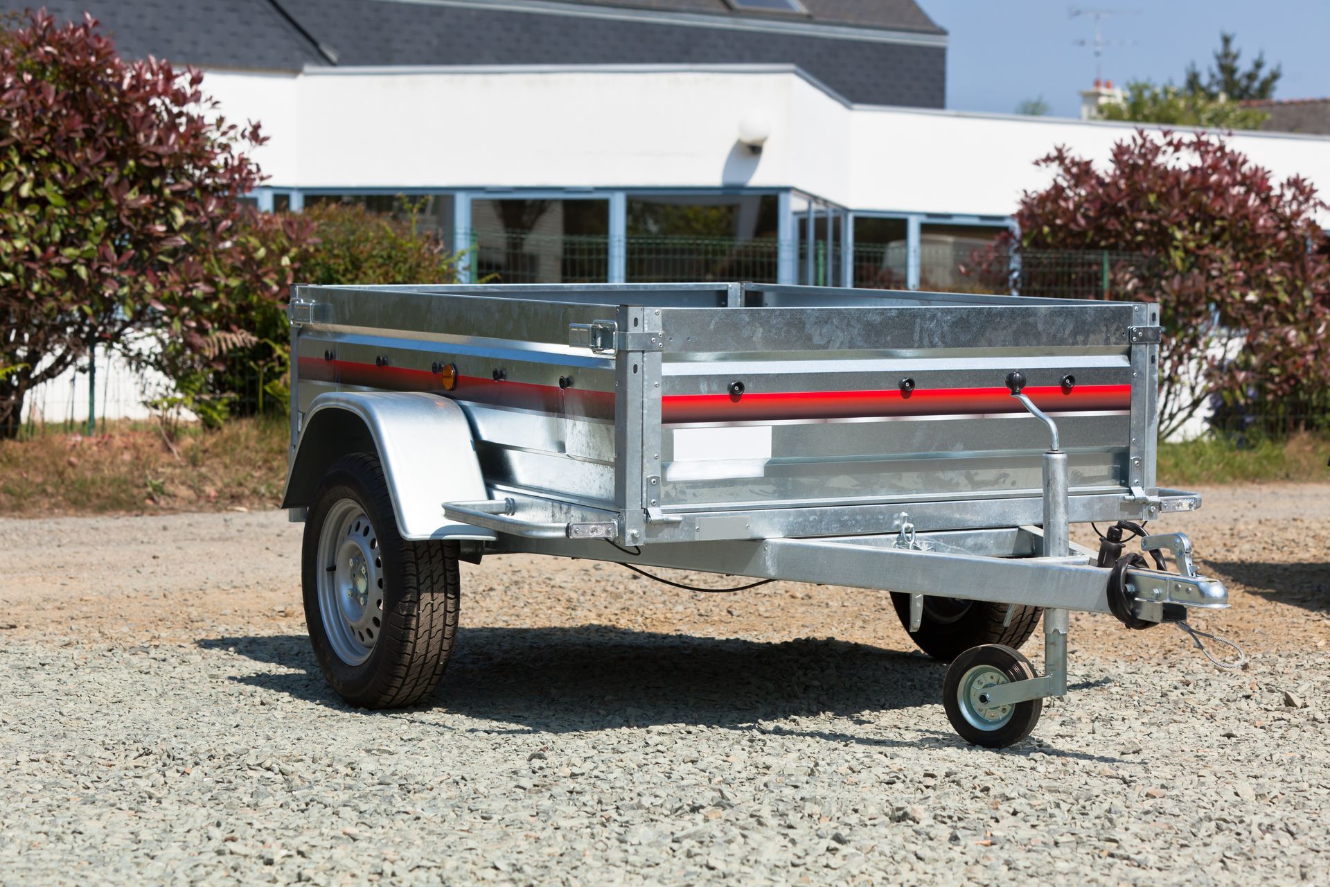 Galvanized metal utility trailer with red accents parked on gravel.
