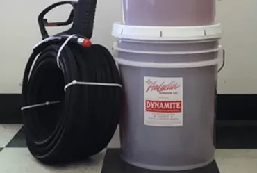Black hose coiled next to a bucket of purple liquid labeled