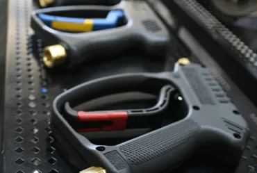 Black pressure washer guns with colored trigger guards in a tray.