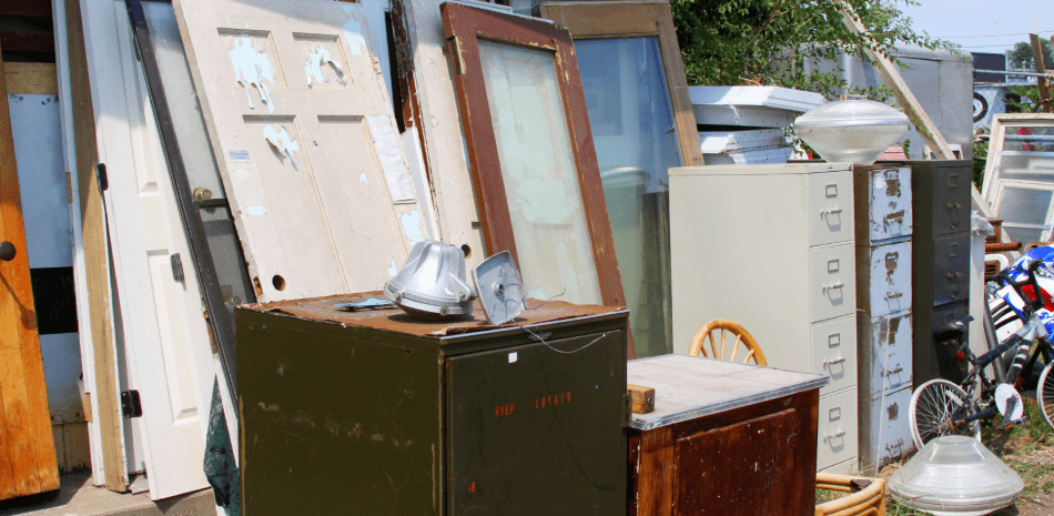 A collection of doors, windows, and other items displayed outdoors, likely for sale at a yard sale.