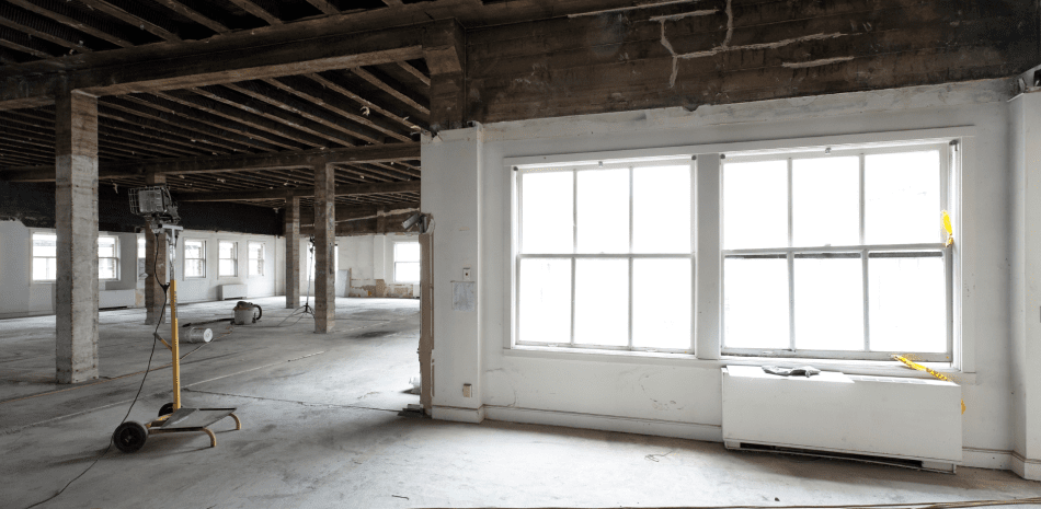 Interior of a large, empty room with exposed wooden beams and columns, and large windows.