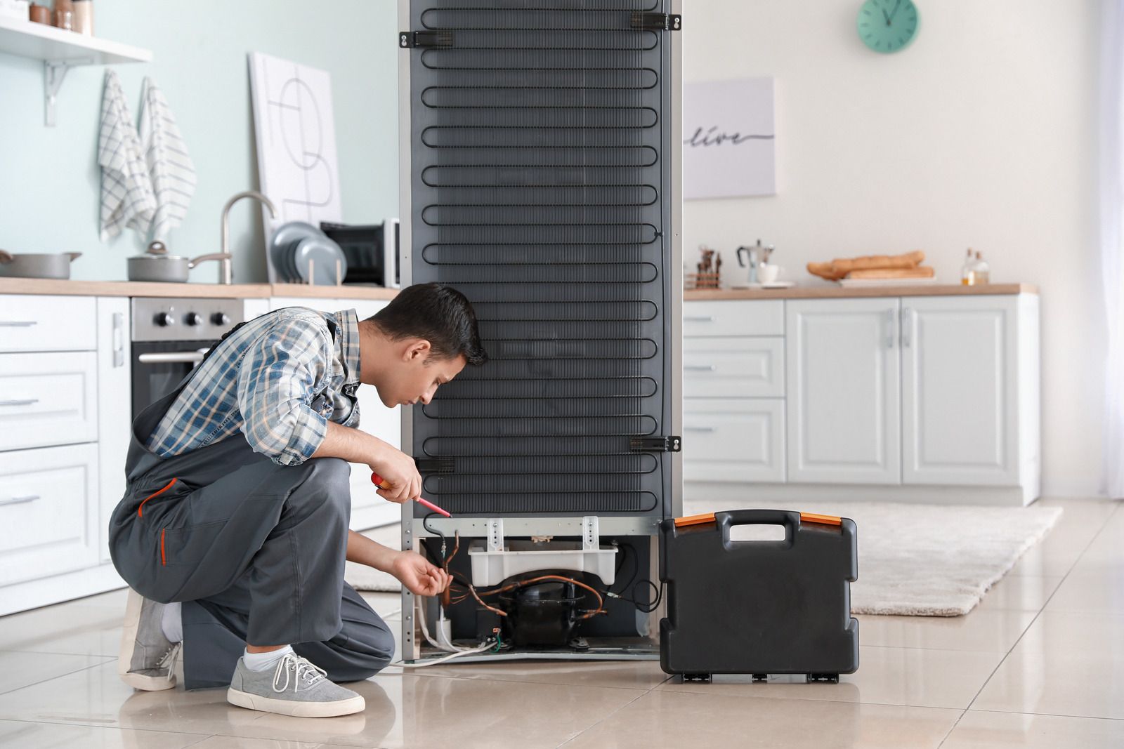 A man is repairing a refrigerator in a kitchen.
