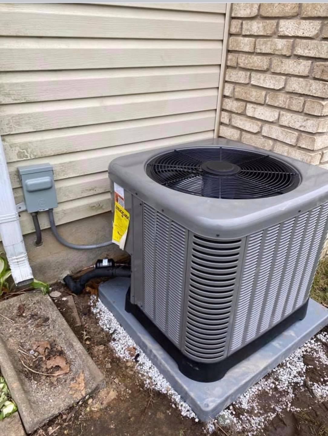 An air conditioner is sitting outside of a house next to a brick wall.