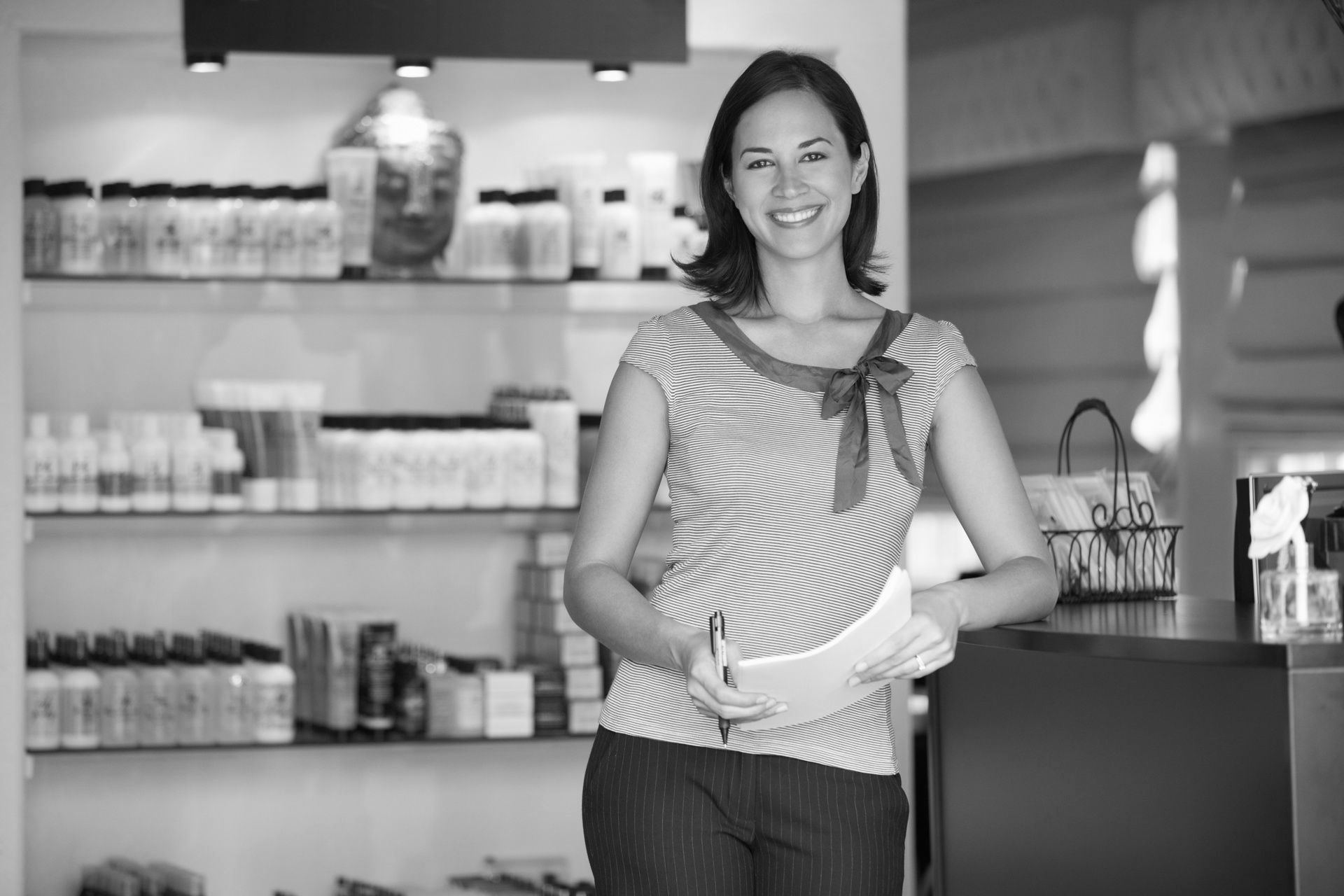A woman is standing in front of a counter in a store holding a piece of paper.