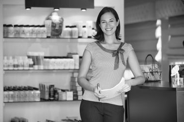 A woman is standing in front of a counter in a store holding a piece of paper.