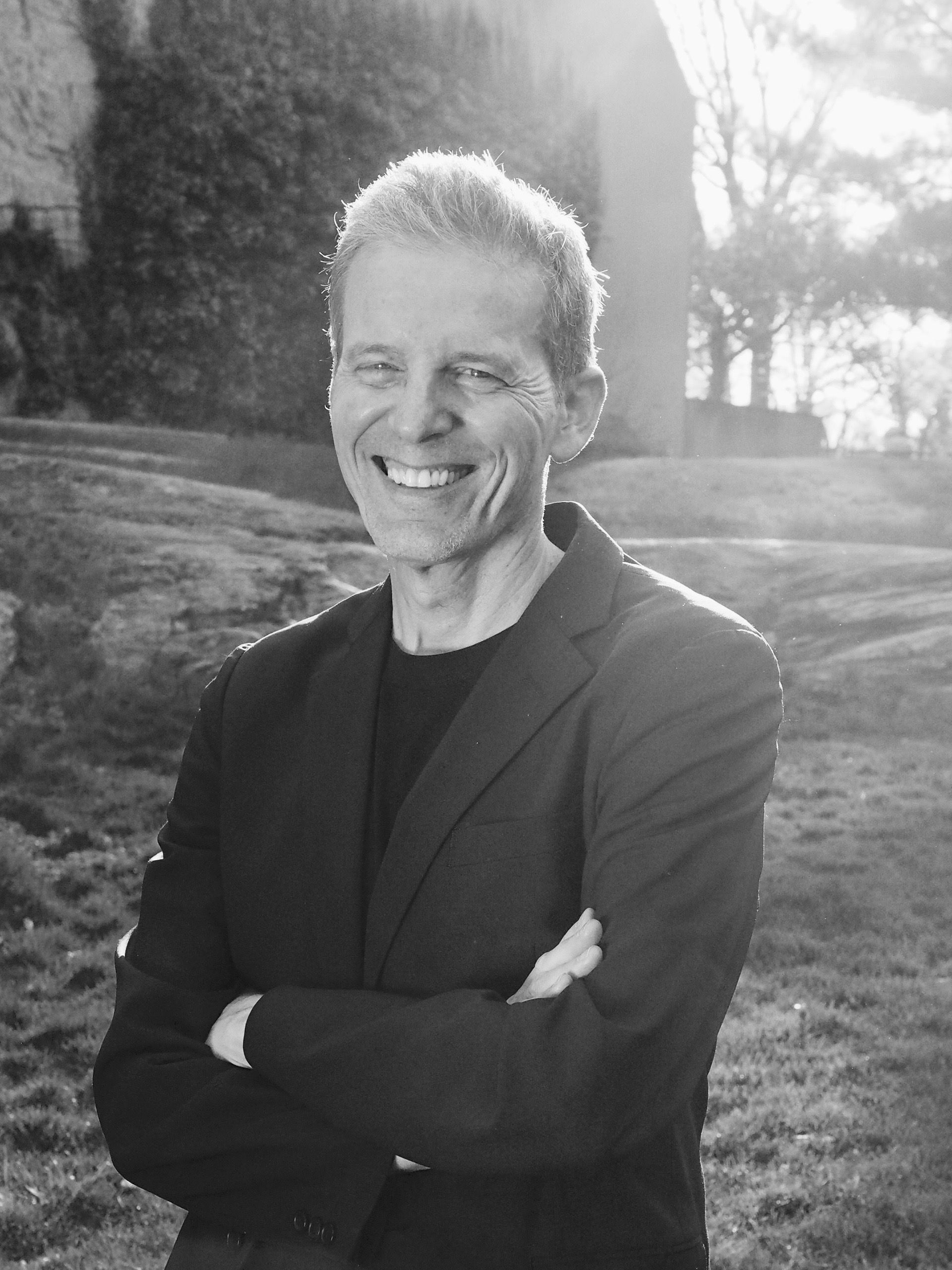 A man in a suit is smiling with his arms crossed in a black and white photo.