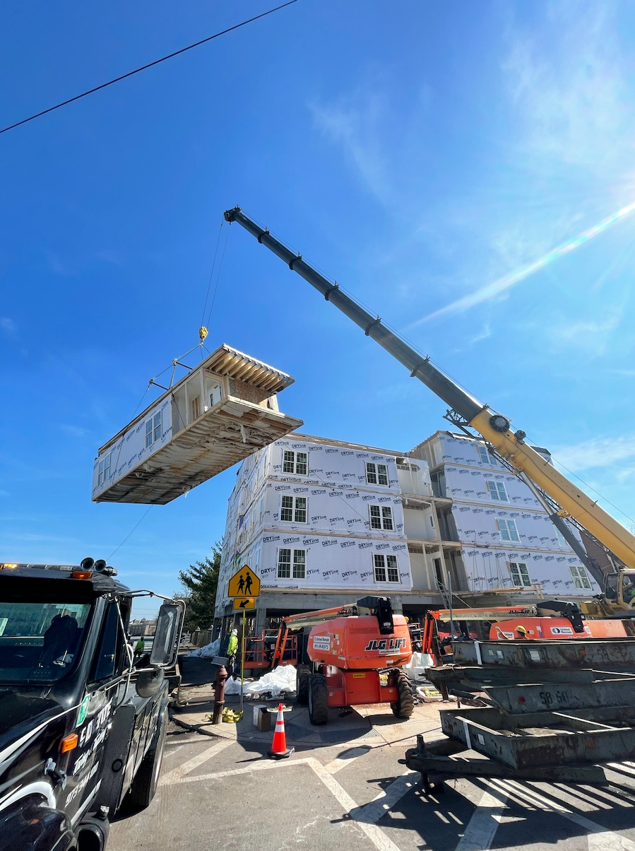 A crane is lifting a house into place on top of a building.