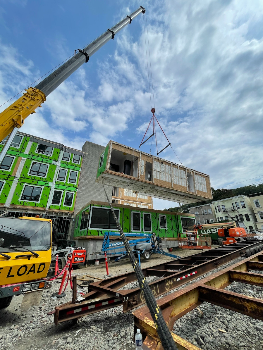 A crane is lifting a piece of wood in front of a building under construction.