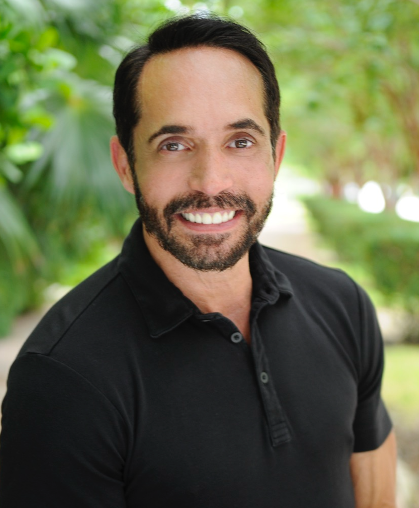 A man with a beard is wearing a black polo shirt and smiling for the camera.