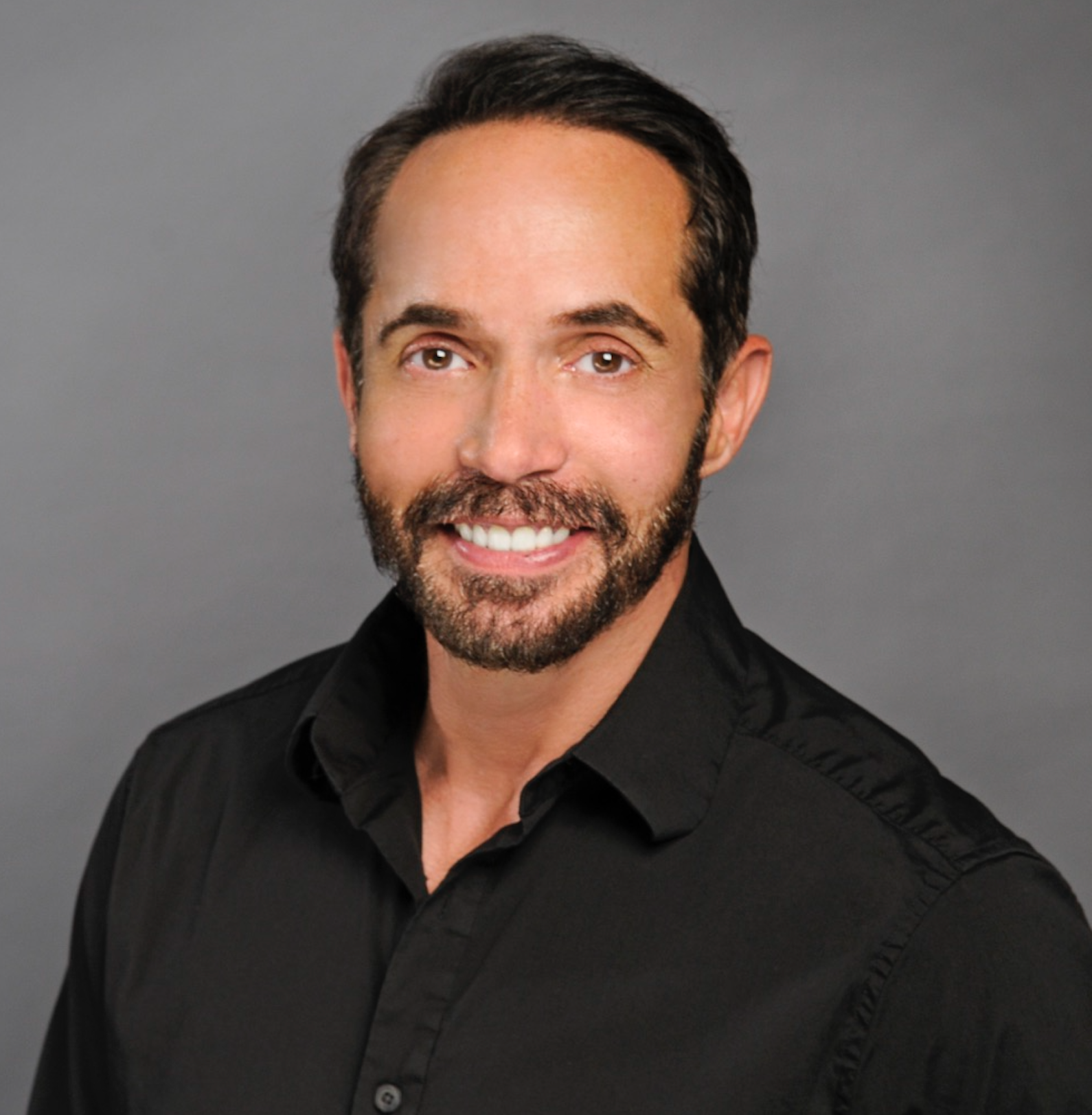 A man with a beard is wearing a black shirt and smiling for the camera.