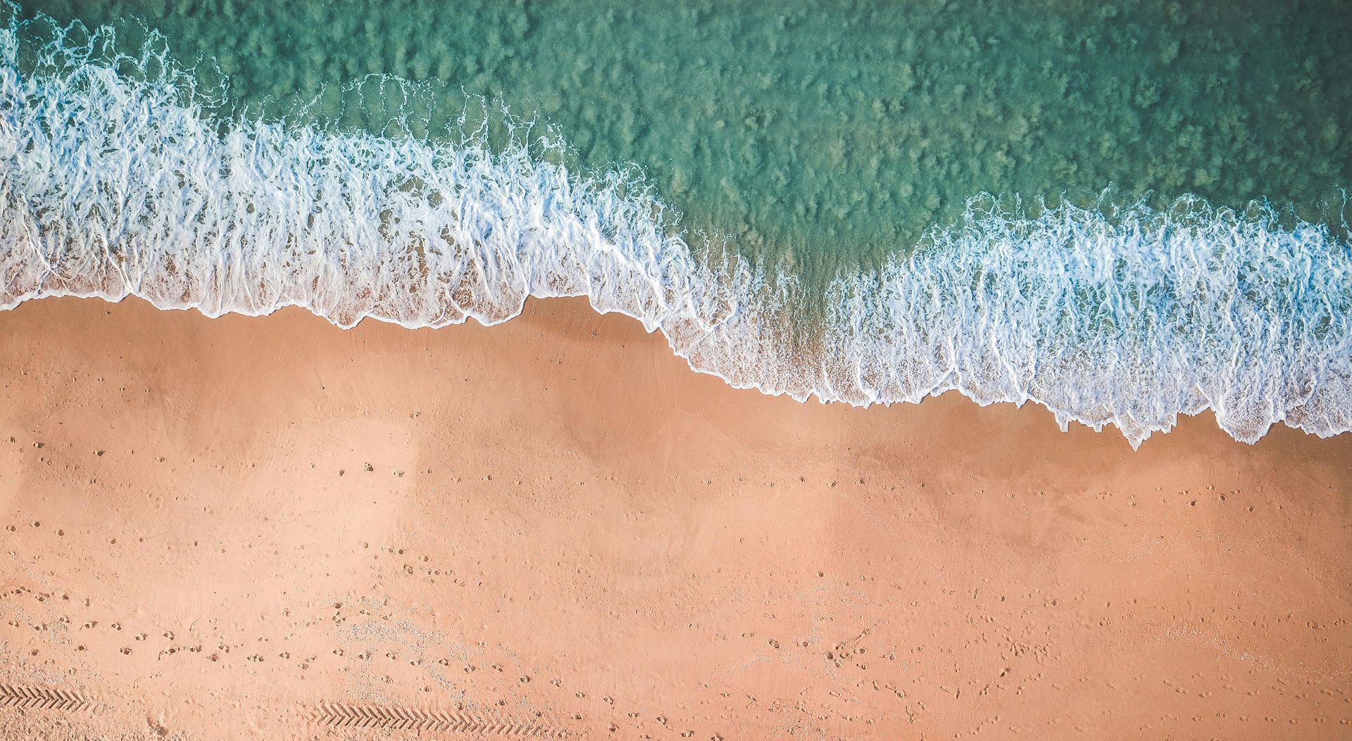 An aerial view of a beach with waves crashing on the sand.