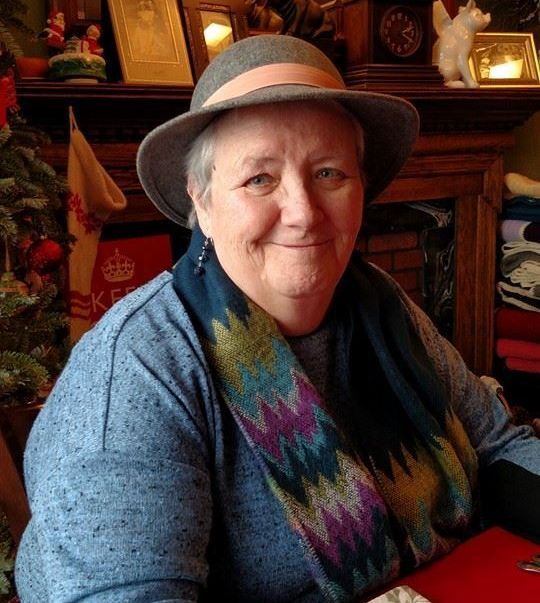 Woman with gray hat and scarf smiles indoors.
