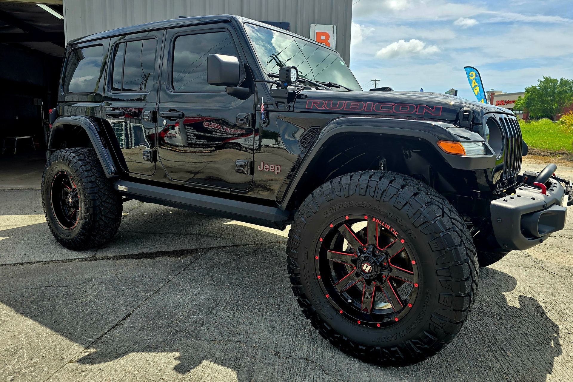 A black jeep wrangler with red wheels is parked in front of a building.