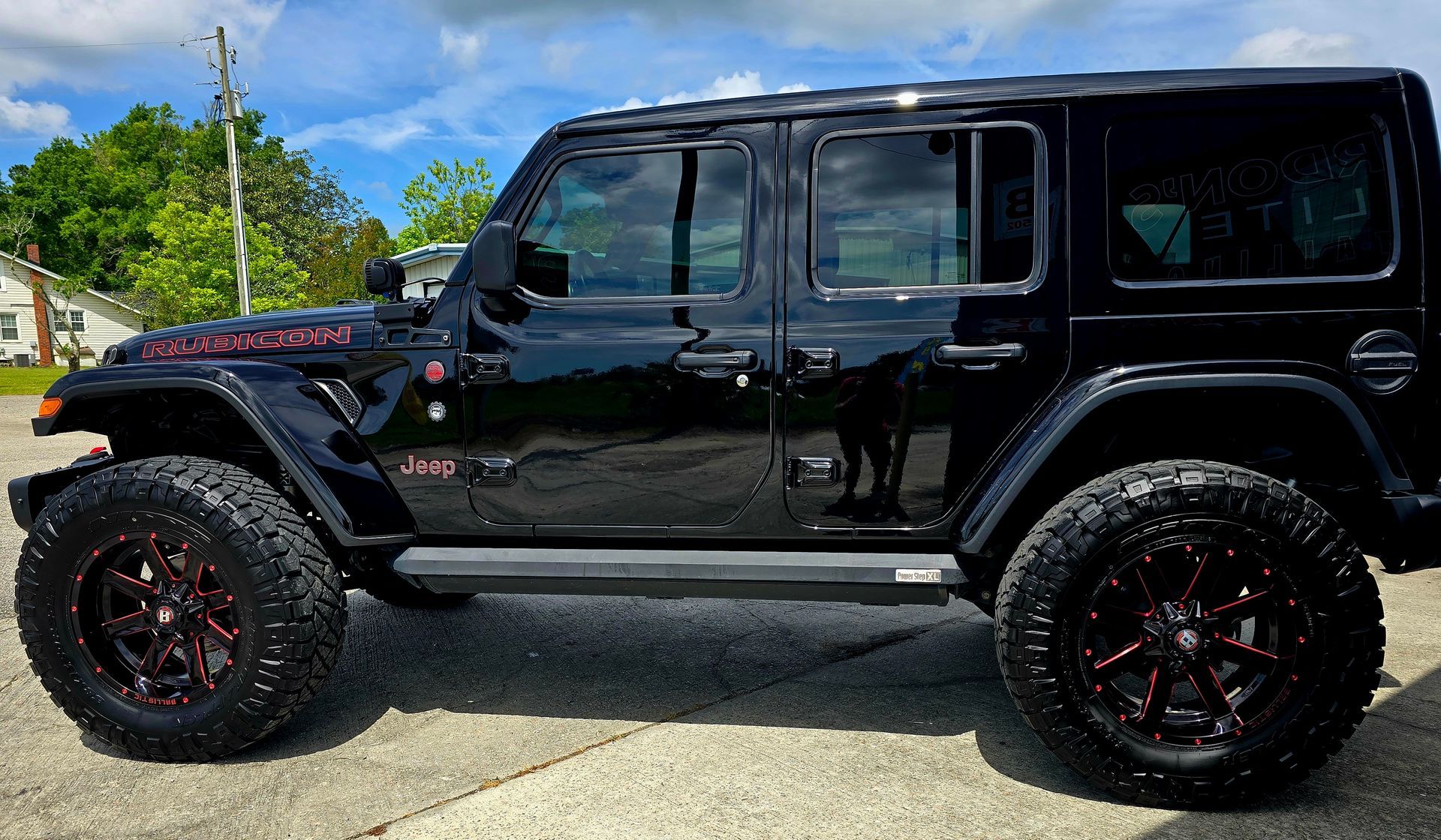 A black jeep wrangler with red wheels is parked in a parking lot.