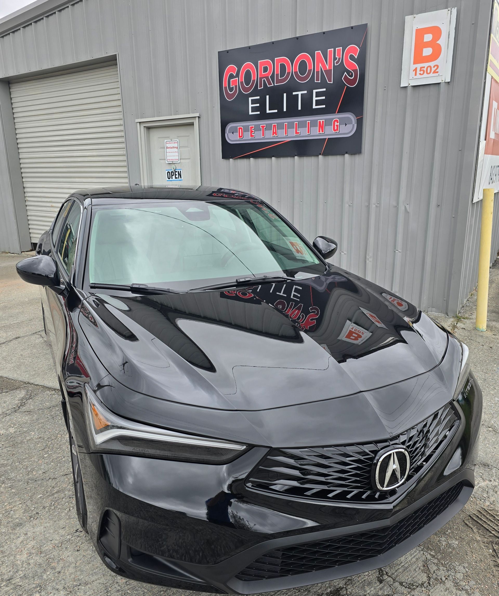 A black car is parked in front of a building with a sign that says gordon 's elite.