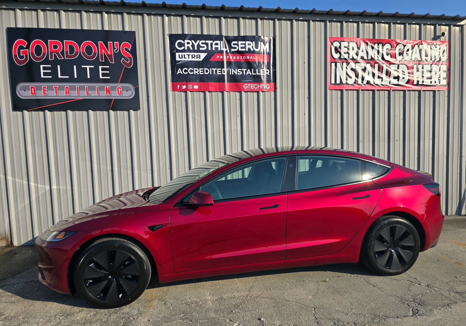 A red tesla model 3 is parked in front of a building.