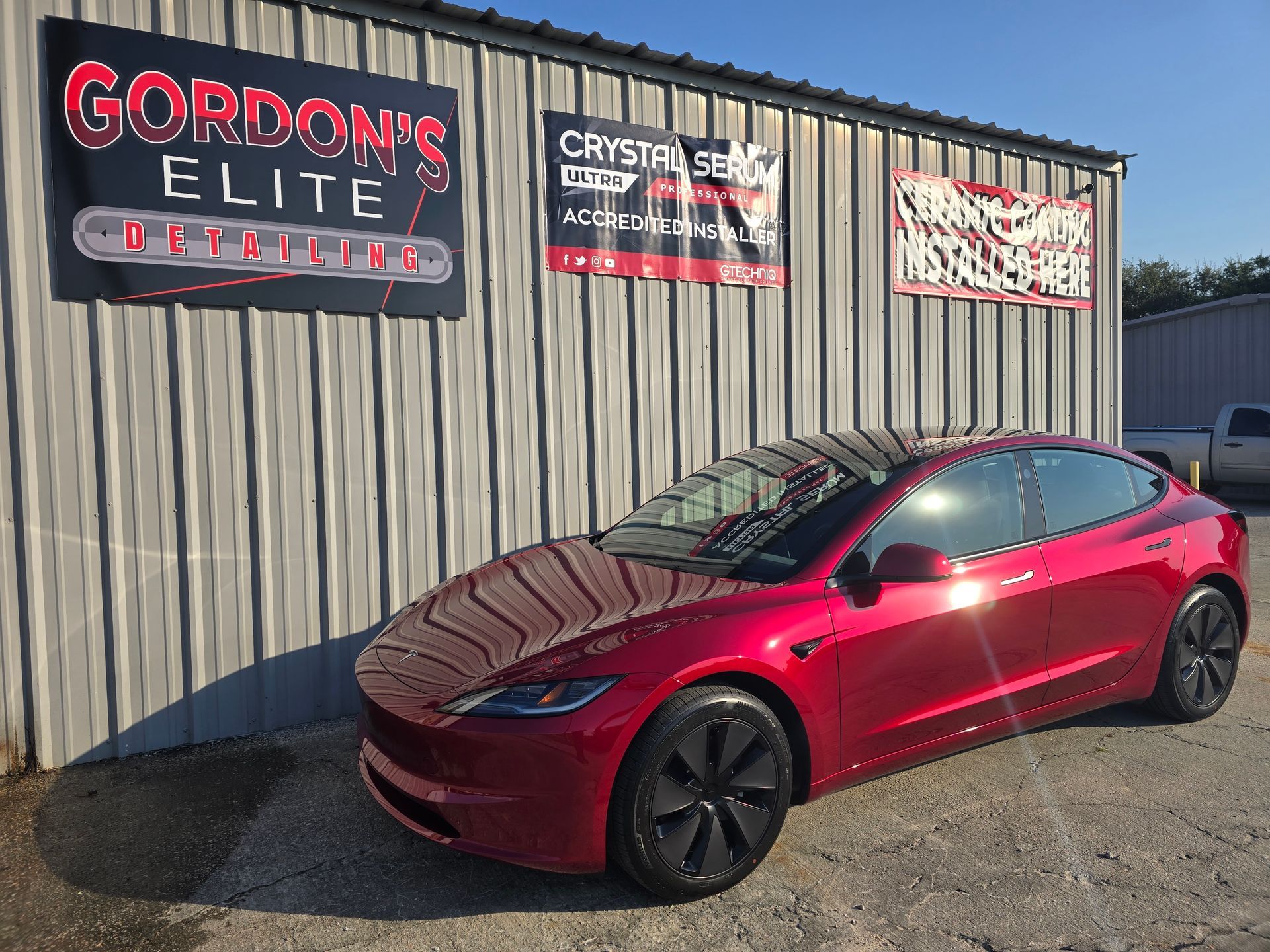 A red tesla model 3 is parked in front of a building.