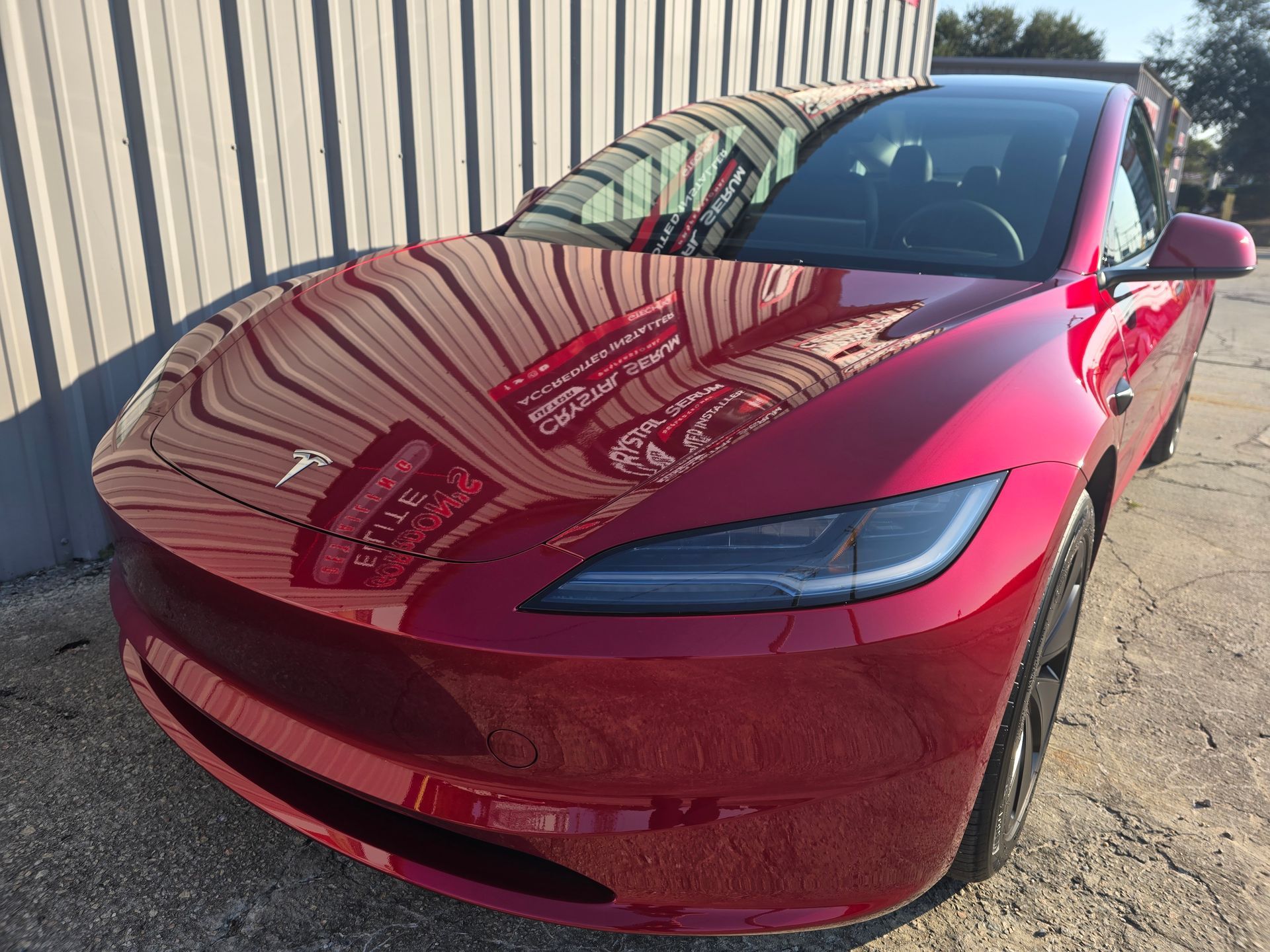 A red tesla model 3 is parked in front of a building.