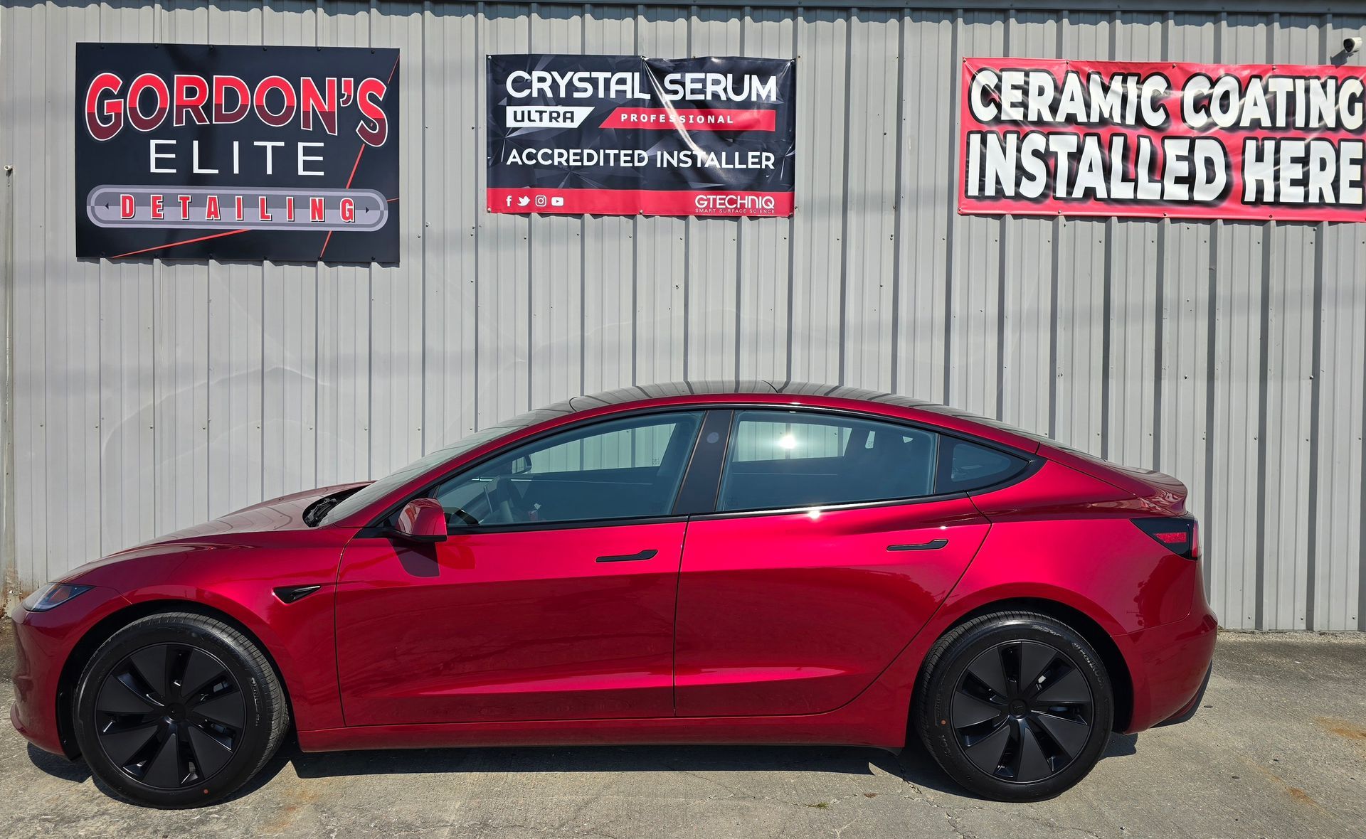 A red tesla model 3 is parked in front of a building.