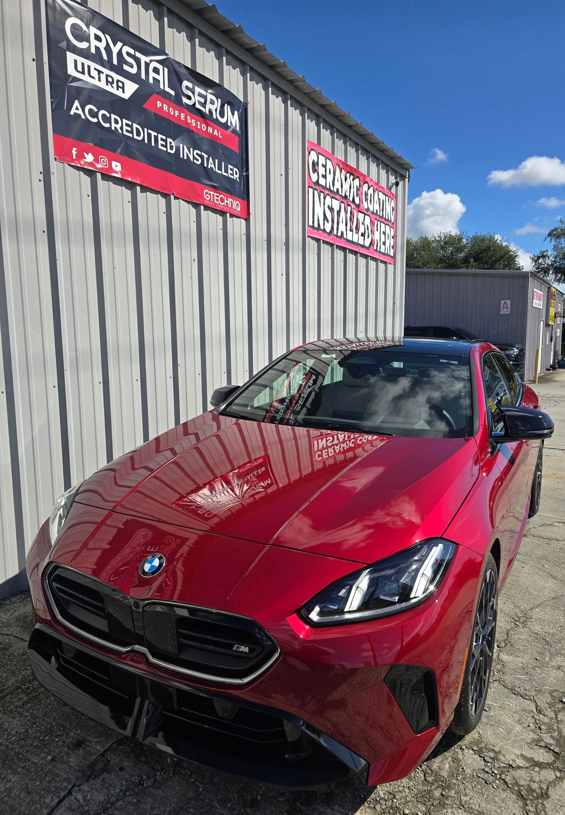 Red BMW coupe parked outside a building with signs. Sunny day.