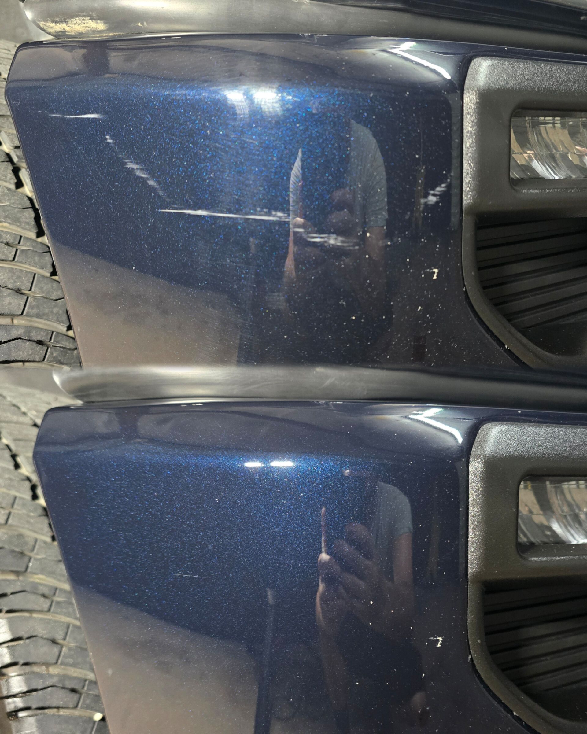 A blue car with a reflection of a person taking a picture