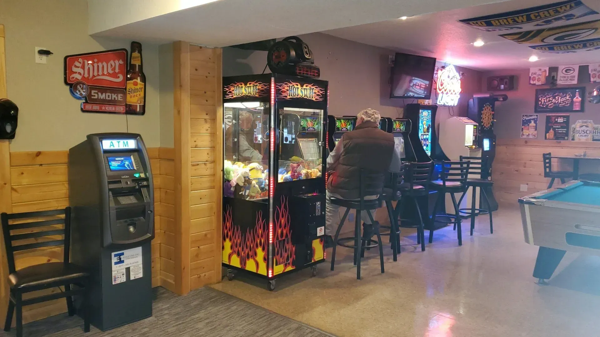 An ATM near a man is sitting at a bar playing arcade games.