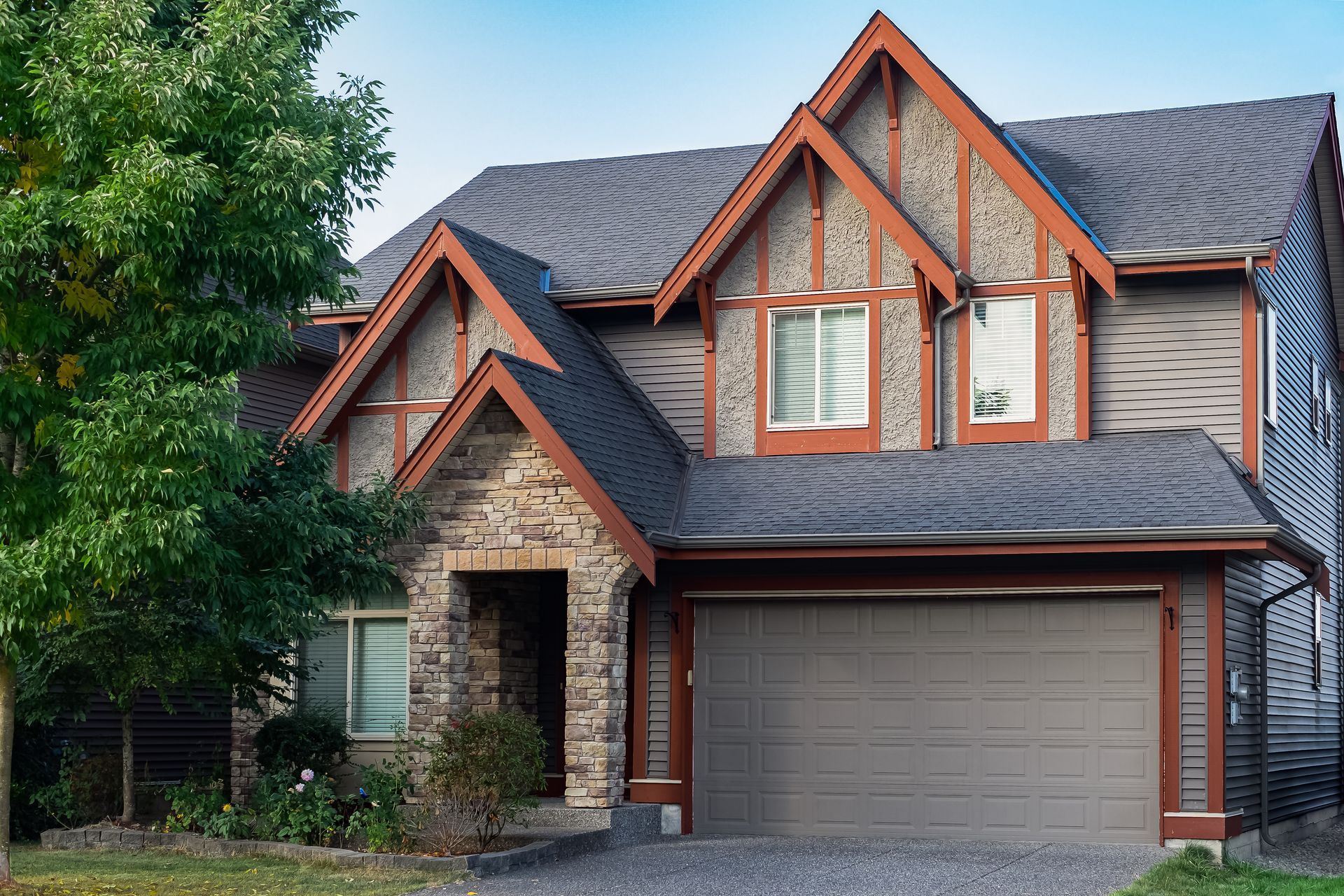 Two-story house with stone facade and gray roof, brown trim, and a closed garage door.