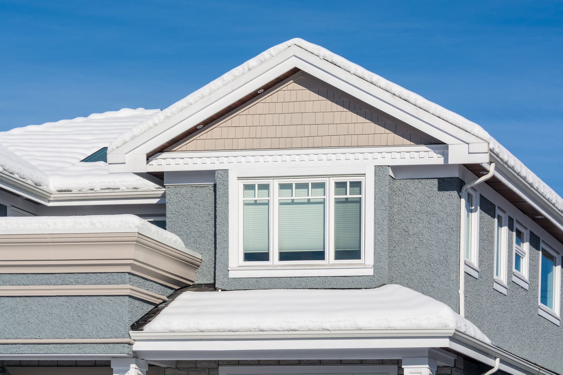 Snow-covered house with a gray exterior, white trim, and a blue sky in the background.