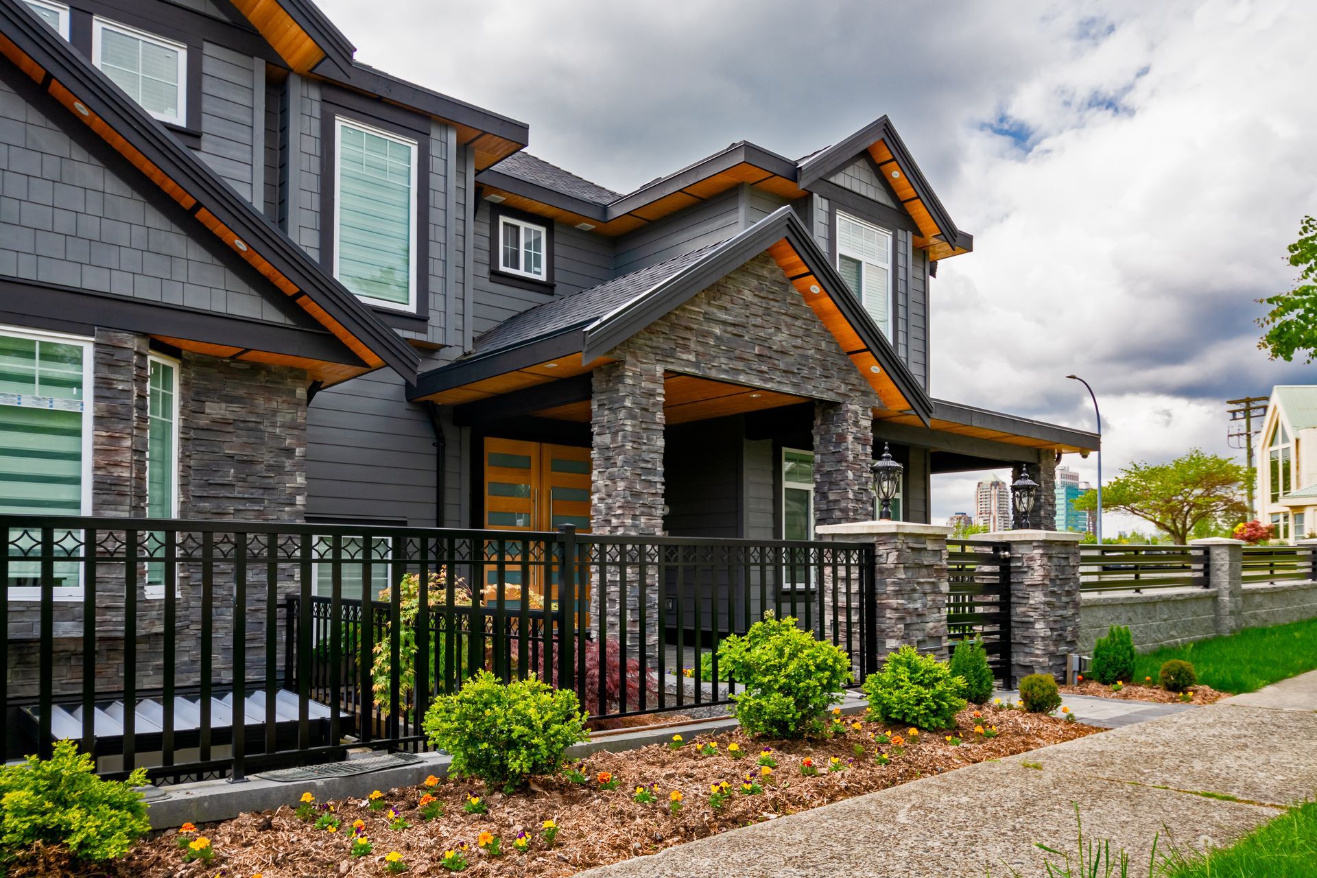 Modern gray house with stone accents, black fence, and landscaped yard.