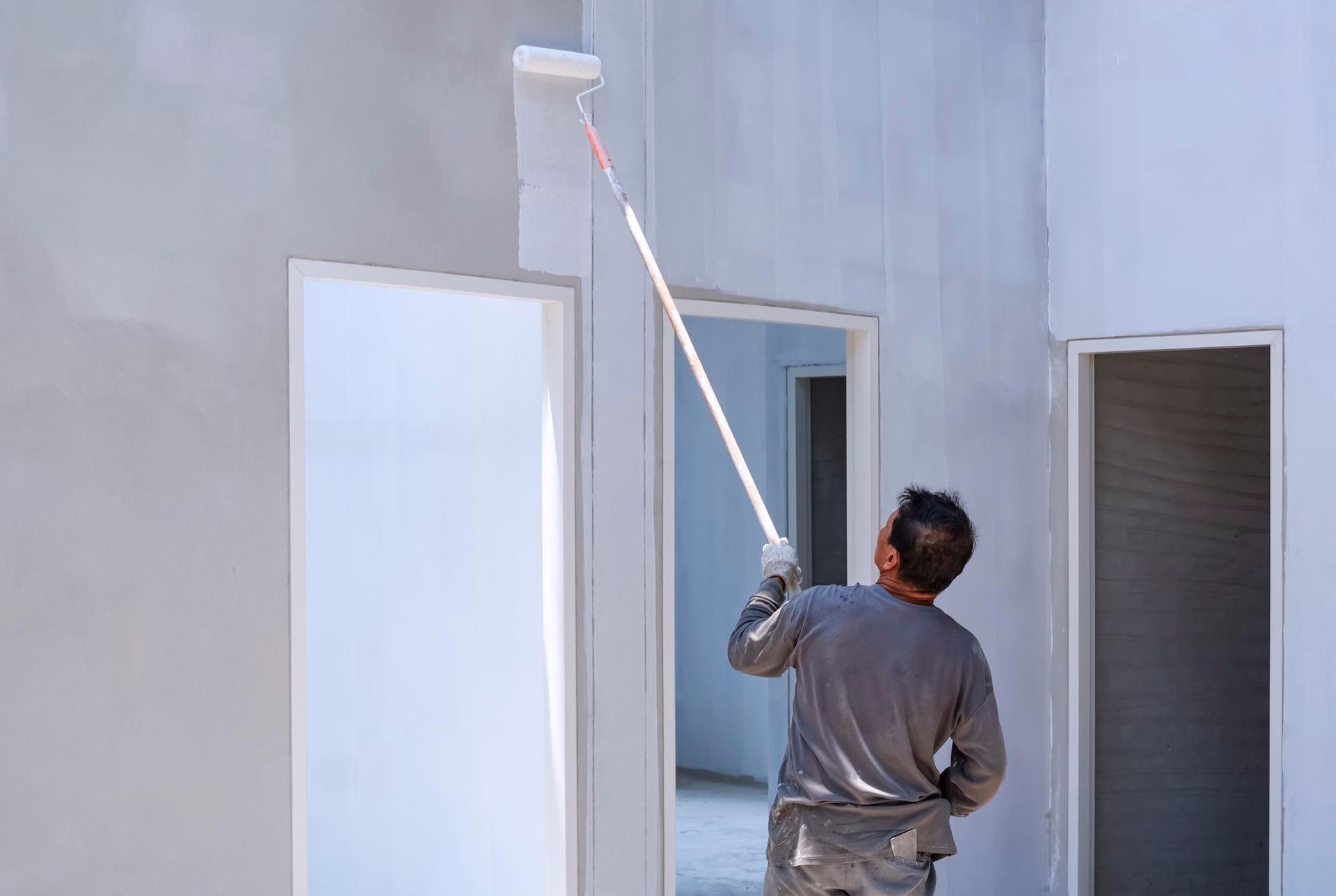 A man is painting a wall with a paint roller.