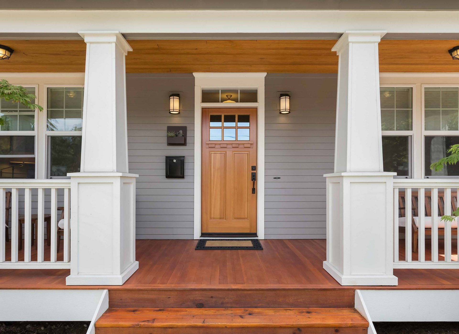 the front porch of a house with a wooden door and white pillars .