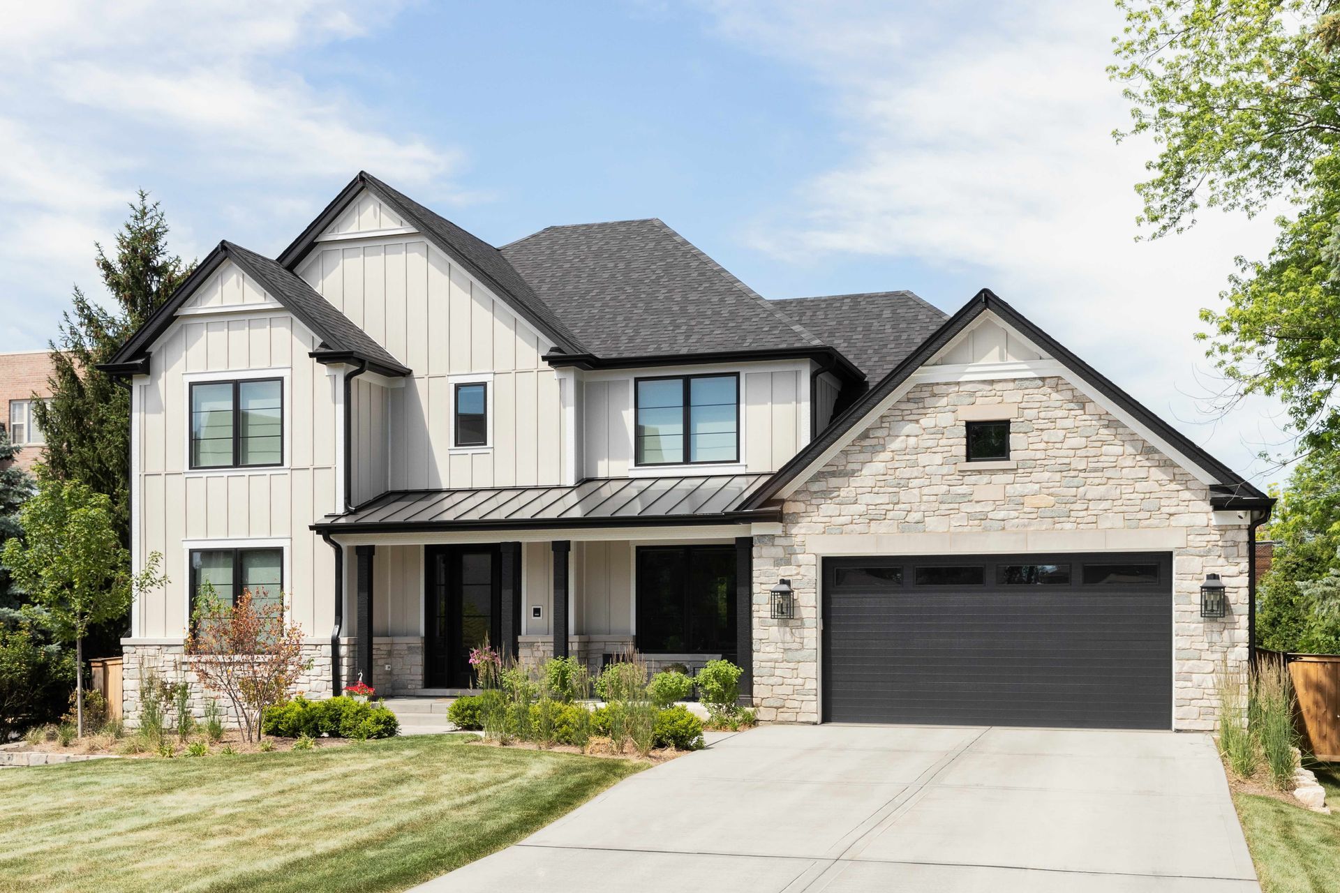 a large white house with a black garage door is sitting on top of a lush green lawn .