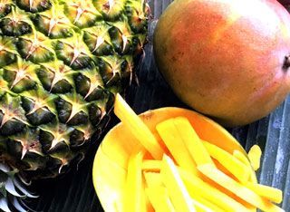 A pineapple , mango and a bowl of mango slices on a table.