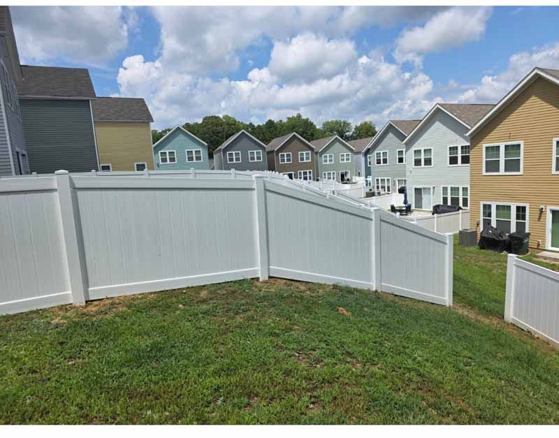 White vinyl fence around a grassy yard in a suburban neighborhood under a partly cloudy sky