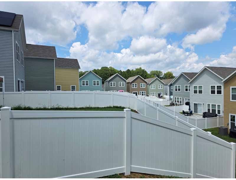 White vinyl fence and suburban townhouses under a partly cloudy sky