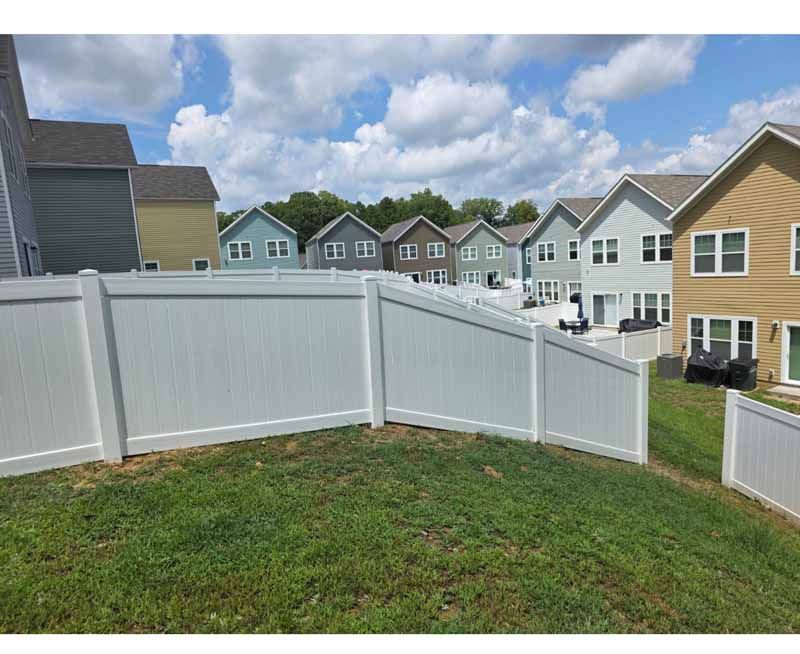 White vinyl backyard fence with a gate beside a grassy yard in a suburban neighborhood.