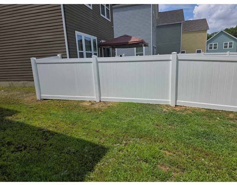 White vinyl privacy fence in a grassy backyard beside a brown house and patio.