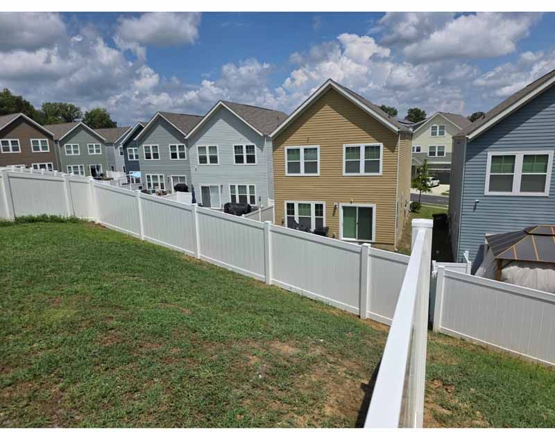 Backyard overlooking row of suburban townhouses beyond a white fence under a cloudy sky