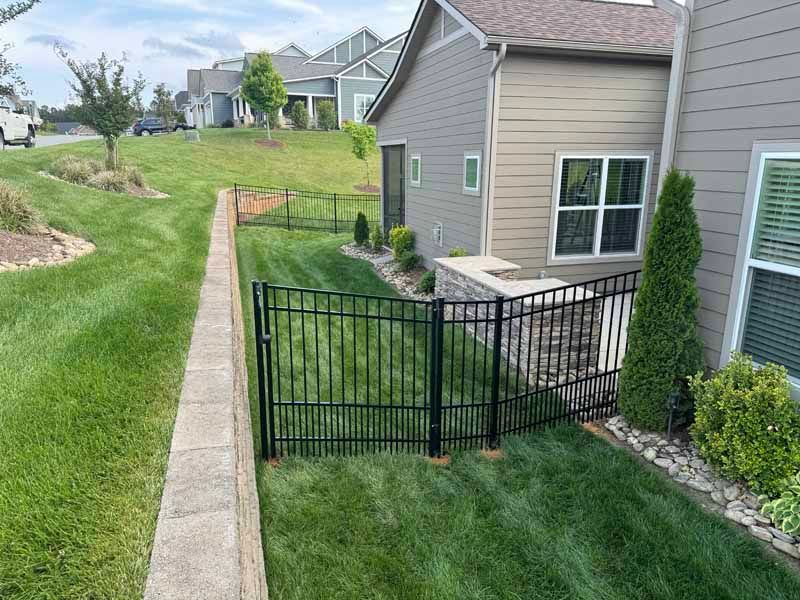Black metal gate beside a townhouse, opening onto a grassy yard and concrete path