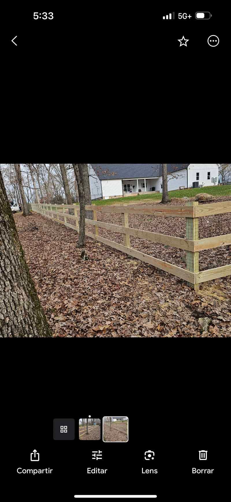Leaf-covered yard with a wooden fence and railing beside a tree and a house in the background