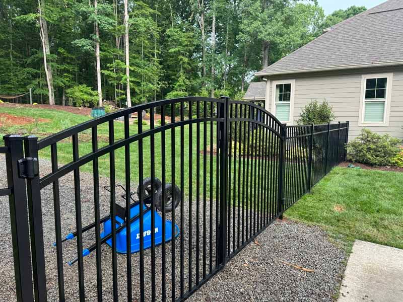 Black metal fence along a gravel path beside a blue tarp-covered object in a suburban backyard.