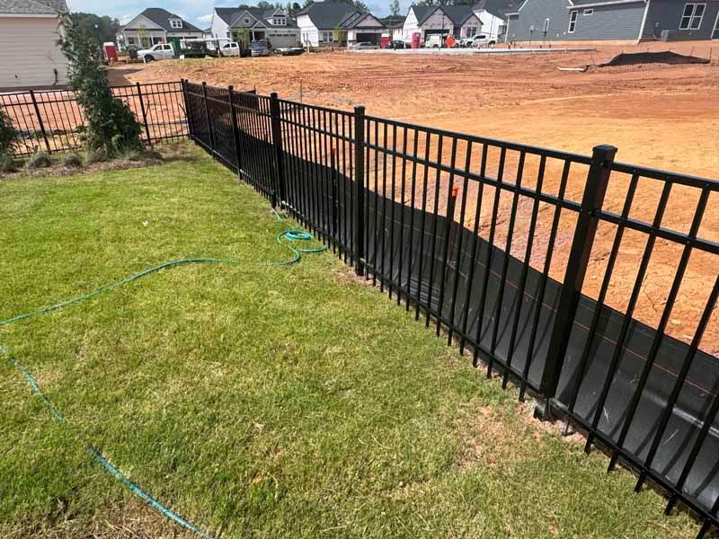Black metal fence along a grassy yard beside a large dirt construction site in a new neighborhood