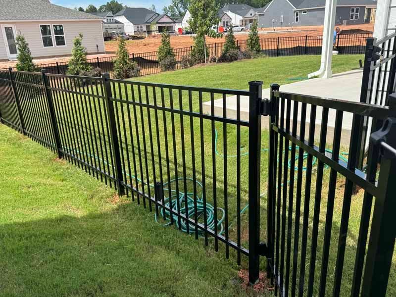 Black metal fence along a grassy yard in a suburban neighborhood