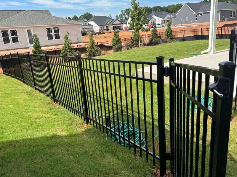 Black metal fence along a grassy backyard with a house and wooden privacy fence in the background