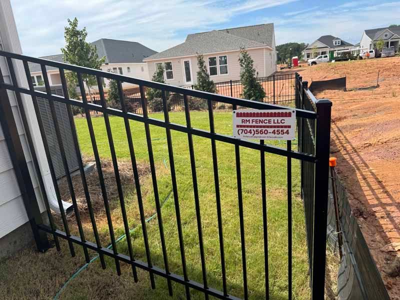 Black metal fence beside a grassy yard and brick construction area with a small warning sign.