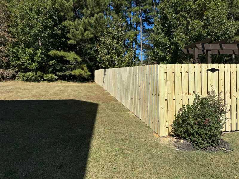 Wooden fence along a sloped backyard with grass, trees, and a small shrub.