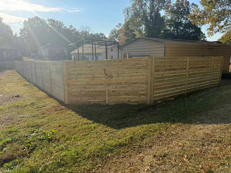 Wooden privacy fence around a backyard shed in bright sunlight