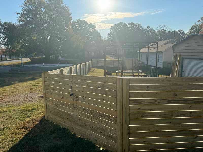 Backyard wooden fence under bright sunlight beside a row of houses and trees