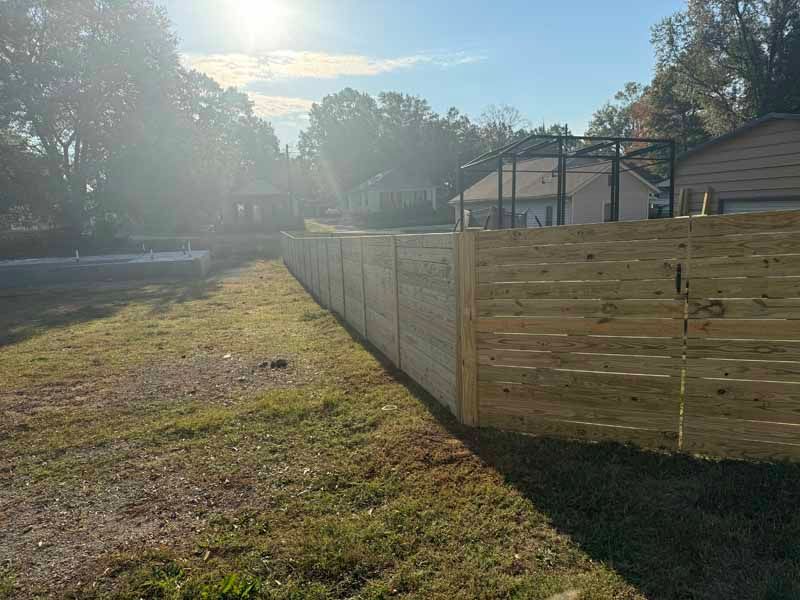 Wooden privacy fence along a grassy yard beside houses in bright sunlight