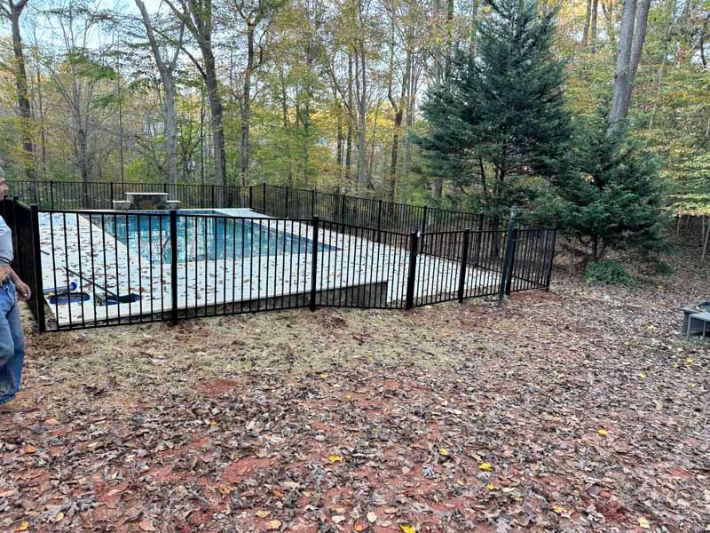Fenced outdoor swimming pool surrounded by autumn trees and fallen leaves